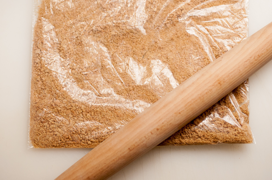 crush graham crackers with rolling pin for pecan pie cheesecake crust