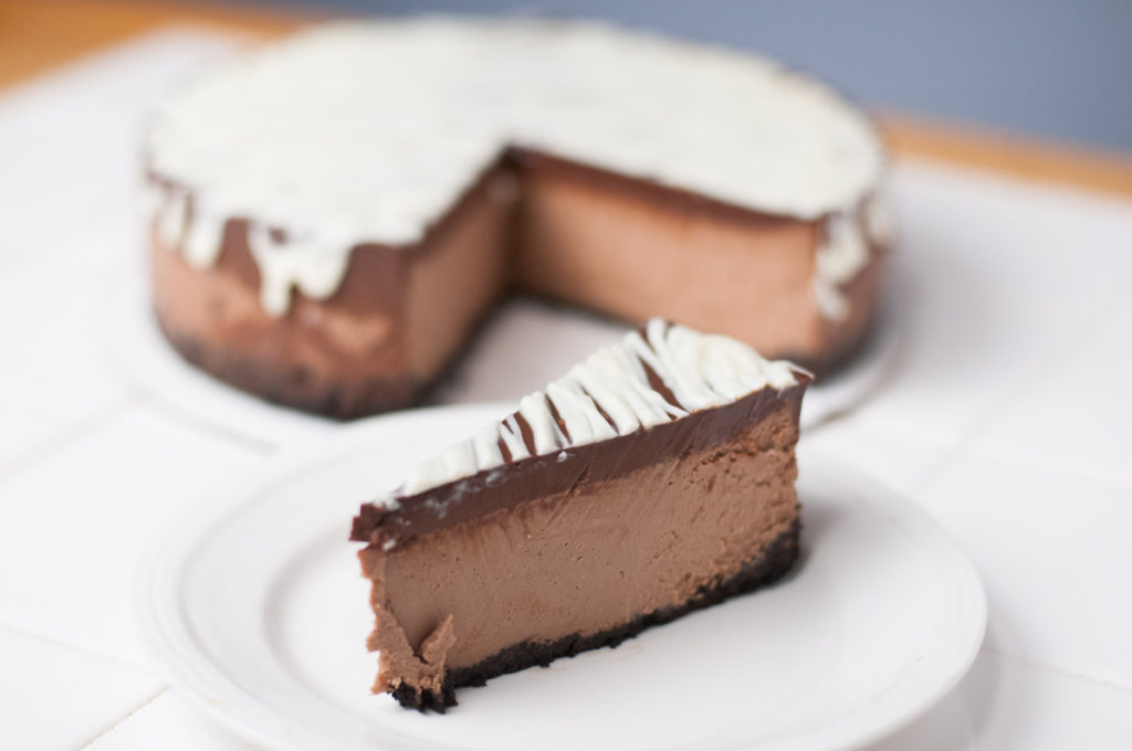 one slice of chocolate to the 4th power cheesecake in front of the entire chocolate to the 4th power cheesecake on white countertop