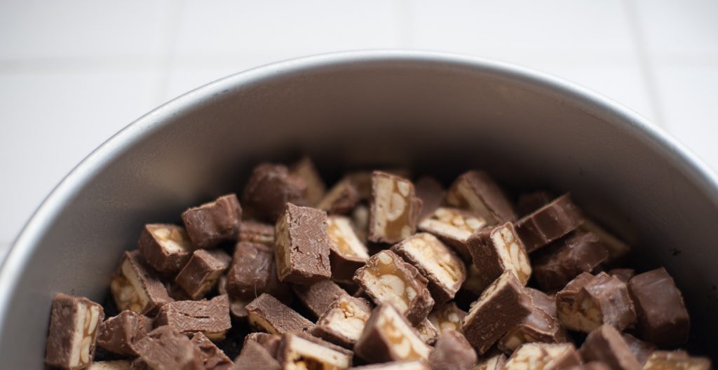 Chopped snickers bars added on top of crust in 9" Fat Daddio cheesecake pan for Snickers cheesecake