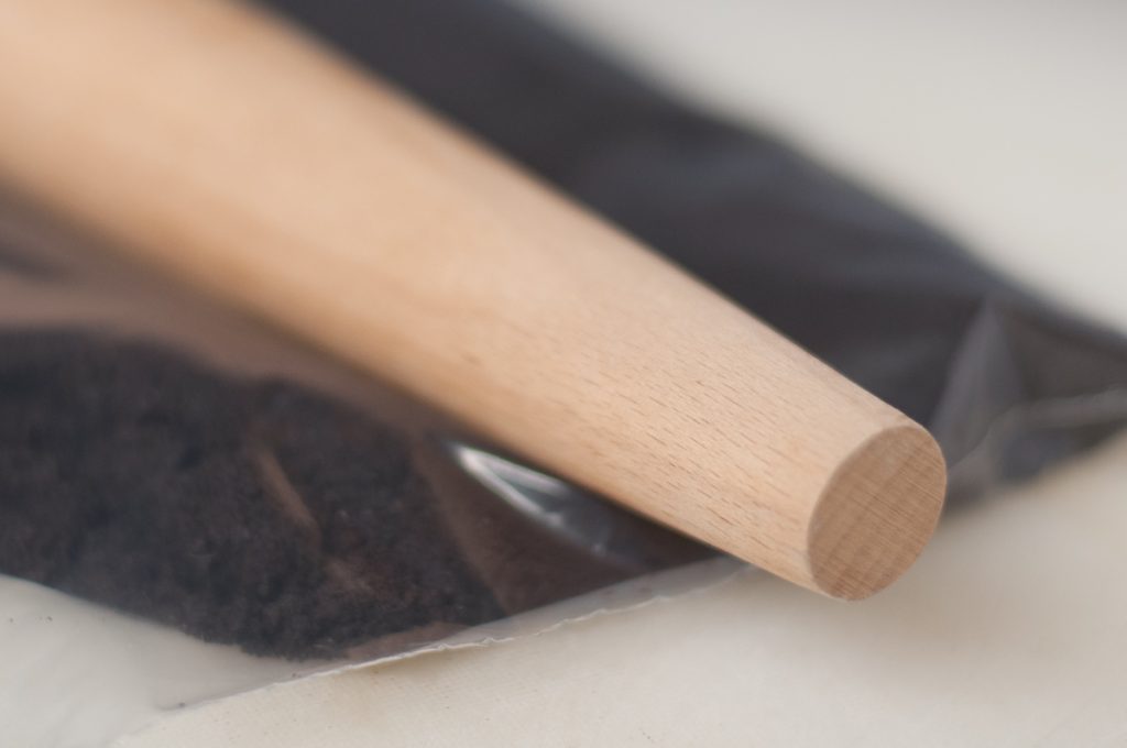 chocolate wafer cookie crumbs in one gallon plastic zip pouch with wooden rolling pin laid on top
