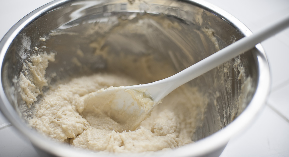 almond shortbread crust ingredients stirred in mixing bowl with plastic mixing spoon,  ready to put into cheesecake pan 