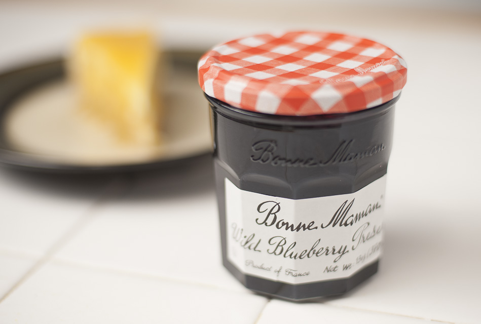 Jar of Bonne Maman Wild Blueberry Preserves in front of ungarnished slice of lemon lemon tart cheesecake