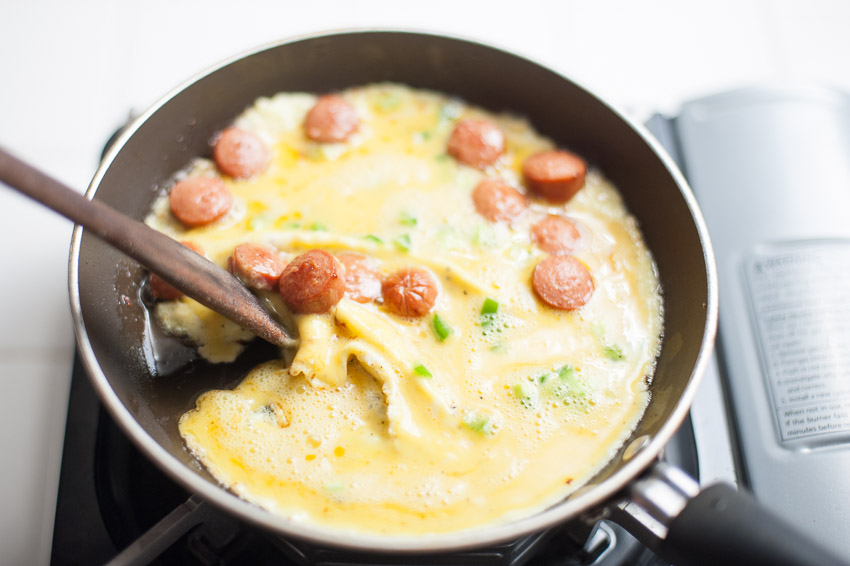 MOVING EDGE OF EGGS AWAY FROM THE SIDE OF THE PAN TO COOK EVENLY