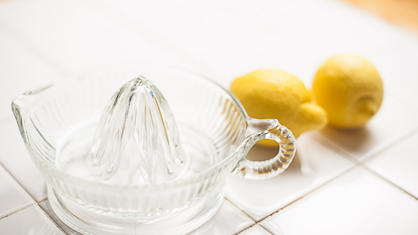 GLASS CGLASS CITRUS JUICER ON TABLETOP NEXT TO TWO LEMONSITRUS JUICER